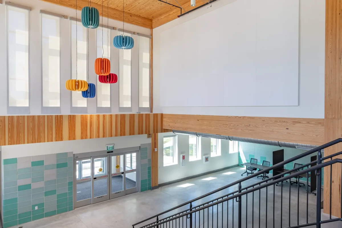 Double-height entry atrium with colorful pendant lights, wood ceiling, and concrete staircase