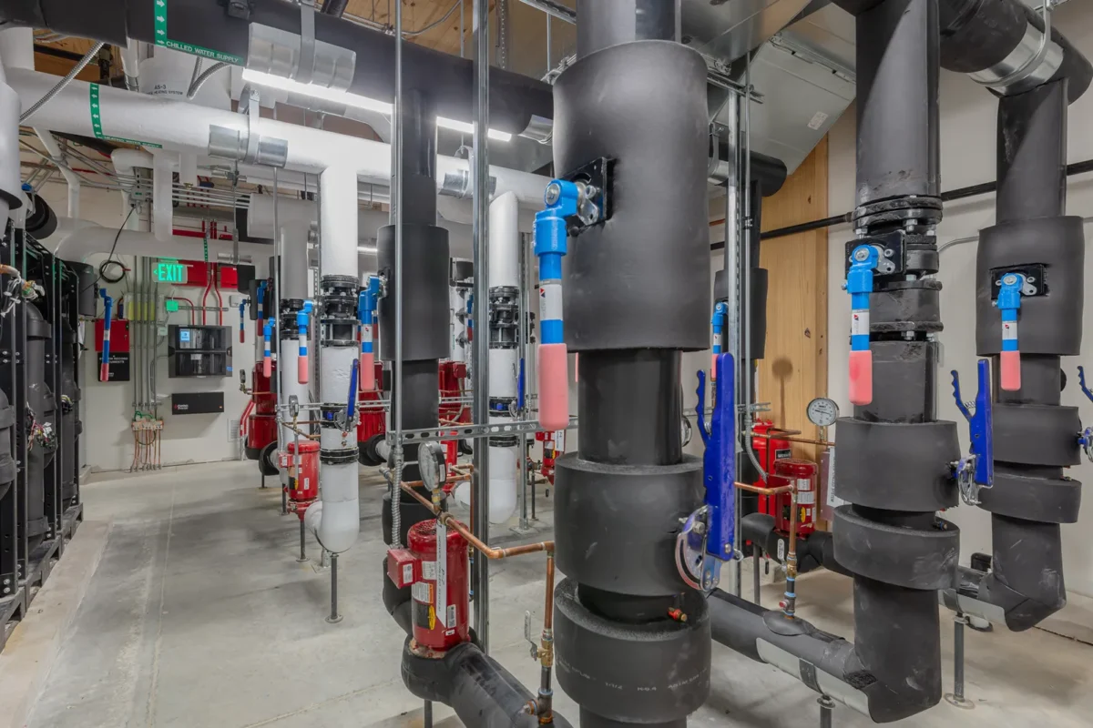 Mechanical room with insulated piping, blue valves, red pumps, and chilled water supply lines