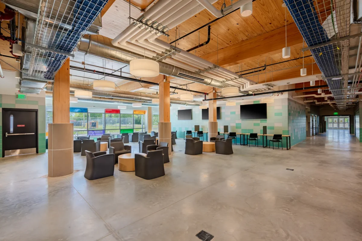 Open lounge with gray armchairs, wood ceiling beams, and teal tile walls in modern building